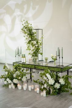 a table with candles, flowers and greenery on it in front of a wall