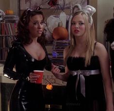 two women dressed up in costumes and holding cups with halloween decorations on the wall behind them