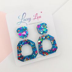 a pair of colorful earrings on top of a white card next to a pink and blue background