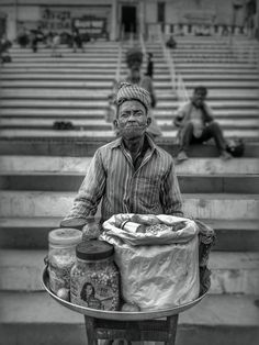 a black and white photo of a man carrying food on a cart in front of some steps