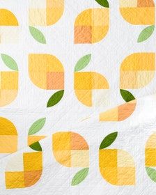 a quilted wall hanging with oranges and green leaves on white fabric, which has been cut in half