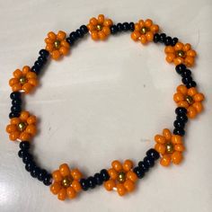 an orange and black beaded necklace on a white surface with gold balls in the shape of flowers