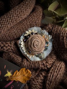 a brown knitted sweater with a flower brooch sitting on top of it next to a book