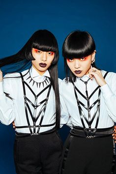 two women with black hair and white shirts are posing for the camera, both wearing suspenders