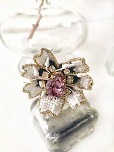 a pink and white flower brooch sitting on top of a glass vase filled with water