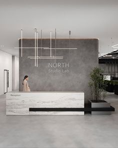 a woman standing in front of a white marble reception desk with the words north studio lab on it