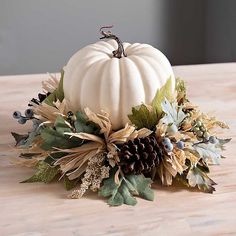 a white pumpkin sitting on top of a wooden table next to leaves and pine cones