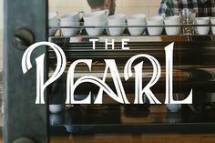 the logo for the pearl coffee house is reflected in the glass door as two men are working behind it