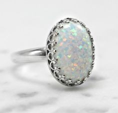 "This gorgeous white pinfire opal sits in a sterling silver 14 x 10mm (9/16\" x 3/8\") crown ring bezel that comes in 6, 7, 8, and 9 US ring sizes. The opal is lab-created with tones of sparkle in shades of pink, blue, lavender and green. Please read more about lab-created opals below. Opals are the birthstone of October but they are also known as the gem of choice by most and loved by many. If you have any questions please do not hesitate to contact me. What is a lab-created opal... Lab-created Classic White Opal Ring With Birthstone, Classic White Opal Birthstone Ring, Oval Cabochon White Gold Opal Ring, Oval Cabochon Opal Ring In White Gold, Oval White Gold Opal Cabochon Ring, White Opal Ring As A Gift, White Opal Ring For A Gift, Classic White Cabochon Opal Ring, Elegant White Opal Birthstone Ring