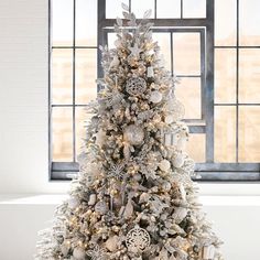 a white christmas tree in front of a window with snowflakes and ornaments on it