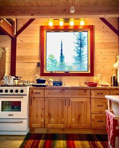 a kitchen with wood paneling and a large window above the stove top, along with an area rug on the floor