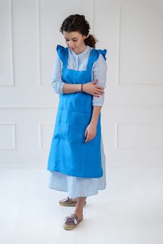 a woman wearing an apron and slippers standing in front of a white wall with her arms crossed