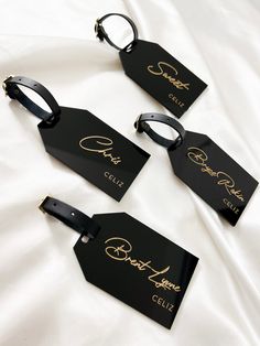 three black tags with gold writing on them sitting on a white bed sheet in front of a white comforter