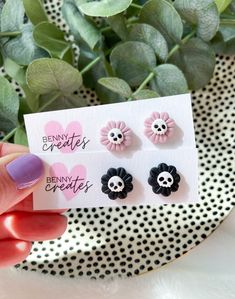 a person holding up three small flower studs on top of a white and black polka dot background