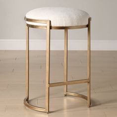 a gold stool with a white cushion on the seat and wooden floor in front of it