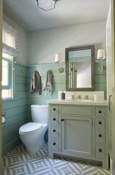 a white toilet sitting under a bathroom mirror next to a sink in a room with blue walls