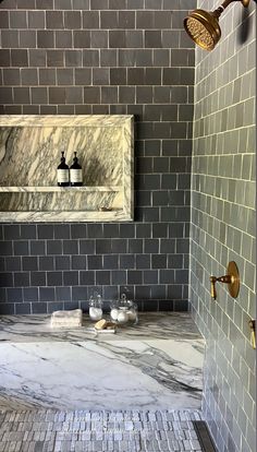 a bathroom with gray tile and gold fixtures on the shower head, two soap dispensers