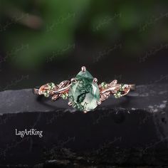 a green stone ring sitting on top of a black piece of wood with leaves around it