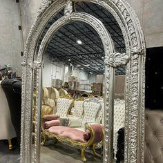 an ornate white and gold mirror sitting on top of a floor next to couches