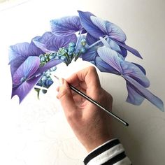 a person is drawing flowers on a piece of paper with a brush and watercolor pencil