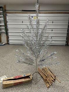 a small white christmas tree sitting on top of a floor next to some wooden sticks