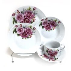 the pink roses are on the white plate and saucer, along with two cups