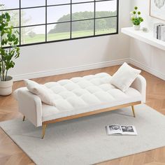 a white couch sitting on top of a wooden floor next to a window in a living room