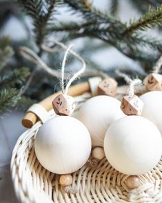 three white ornaments sitting in a wicker basket on a table next to a pine tree