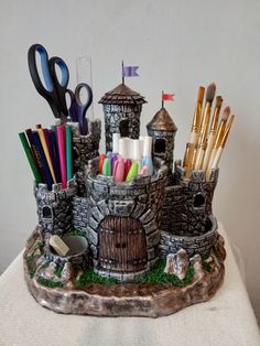 a castle made out of clay with scissors, pens and markers in it on a table