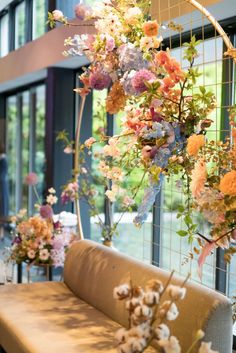 an arrangement of flowers hanging from the ceiling next to a bench in front of large windows