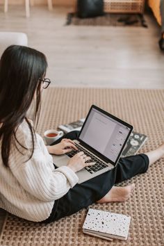 a woman is sitting on the floor with her laptop and coffee in front of her