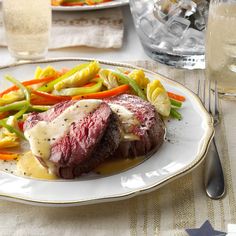 a plate with steak and vegetables on it next to glasses of water, silverware and utensils