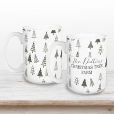 two coffee mugs sitting on top of a wooden shelf with christmas trees printed on them