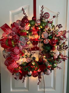 a christmas wreath on the front door with ornaments hanging from it's sides and lights