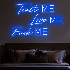 there is a bed with pillows on it and a neon sign that says trust me love me fuk me