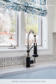 a kitchen sink under a window next to a faucet and windowsill with roman blinds