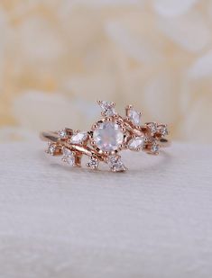 a close up of a ring on a white surface with flowers in the middle and an oval shaped diamond surrounded by smaller round diamonds