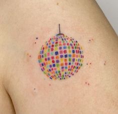 a colorful ball tattoo on the back of a woman's left shoulder, with dots all over it