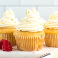 three vanilla cupcakes with white frosting and raspberries on the side