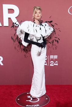 a woman standing on a red carpet wearing a white dress with black feathers around her shoulders