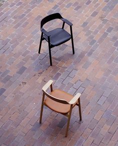 a chair sitting on top of a brick floor next to a black chair with a brown seat