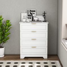 a white dresser sitting next to a potted plant on top of a wooden floor