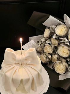 a white cake sitting on top of a table next to a bouquet of flowers and a lit candle