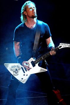 a man with long hair holding a white guitar in his right hand while standing on stage