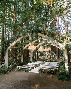 an outdoor ceremony setup with white chairs and chandelier hanging from the ceiling, surrounded by trees