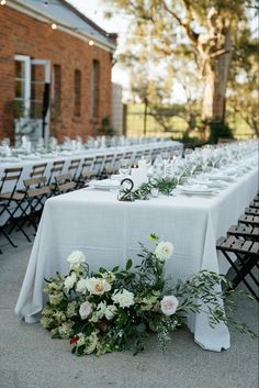 an outdoor table set up with white linens and greenery for a wedding reception