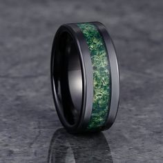 a wedding band with green moss inlays and black ceramic inside, on a gray surface