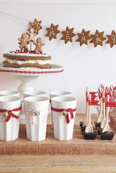 a table topped with white cups filled with desserts and gingerbread men on top of it