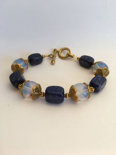 "7.5\"-- 20mm Retangular lapis lazuli gemstone beads and 12mm Opalite Stone beads beautiful statement bracelet, ornate with 15mm brass gold flower caps and a 20mm toggle clasp closure. Hand made jewelry. All purchase will arrive in gifts boxes. Thanks for stopping by!" Blue Lapis Lazuli Gemstone Beaded Bracelet, Sapphire Lapis Lazuli Gemstone Beaded Bracelets, Sapphire Lapis Lazuli Bracelets With Round Beads, Sapphire Gemstone Beads Bracelet In Lapis Lazuli, Sapphire Lapis Lazuli Beaded Bracelets, Sapphire Lapis Lazuli Beaded Bracelet With Natural Stones, Blue Moonstone Beaded Bracelets With Gemstone Beads, Lapis Lazuli Gemstone Beaded Bracelets, Lapis Lazuli Beaded Bracelets With Gemstone