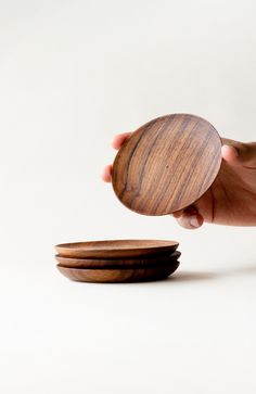 a hand holding a wooden plate over three smaller plates on a white surface with one person's hand reaching for it